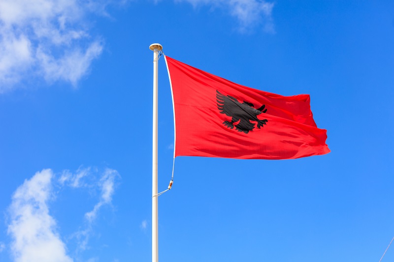Флаг Албании. Албанский флаг на шесте развевается на фоне голубого неба